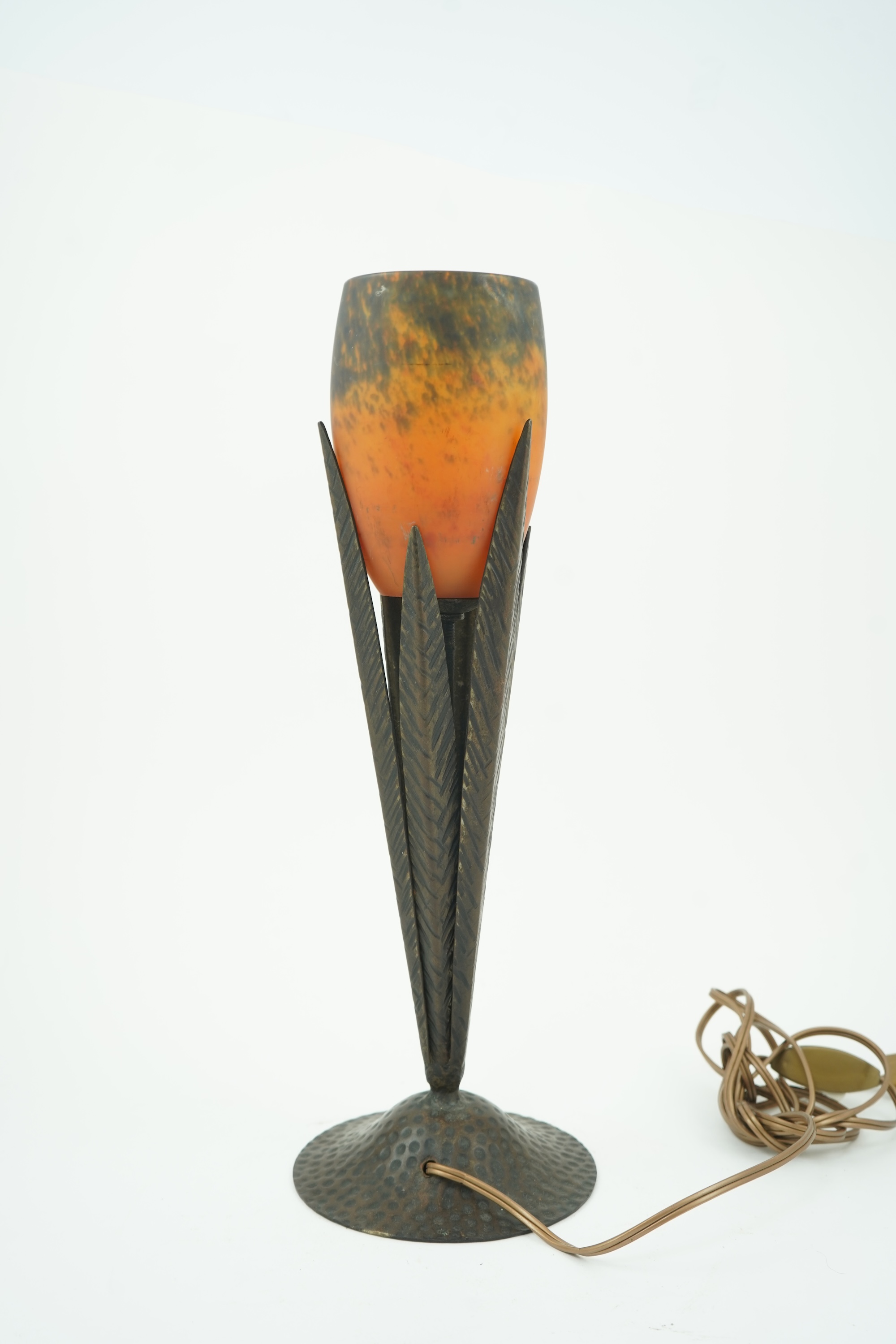 Manner of Muller Freres and Robj: A French Art Deco table lamp the mottled orange glass shade supported by naturalistic palm-leaf metal supports terminating in a circular hammered metal base, 40cm high